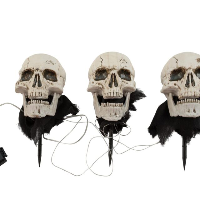 Kolme valaistua Halloween-pääkalloa maapiikeillä