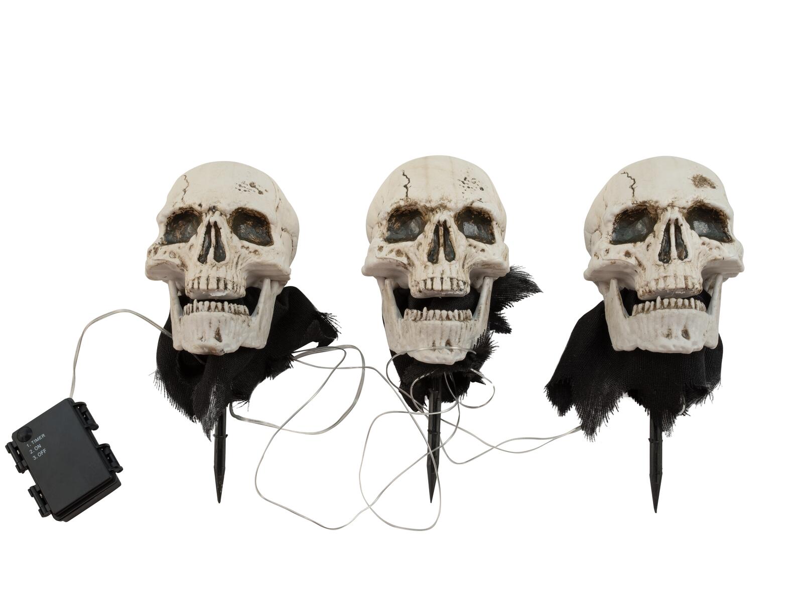 Kolme valaistua Halloween-pääkalloa maapiikeillä